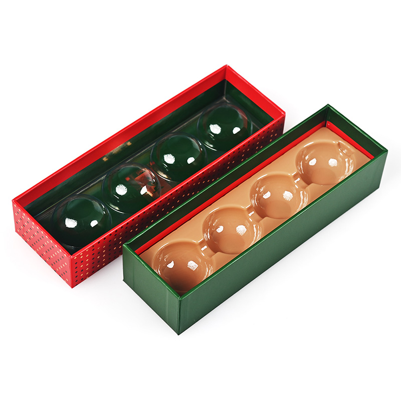 Auseinandergebaute Pralinenschachtel mit rotem Deckel, auf dem sich Plastikkuppeln befinden, sowie grünem Boden mit beigefarbenem Tablett.