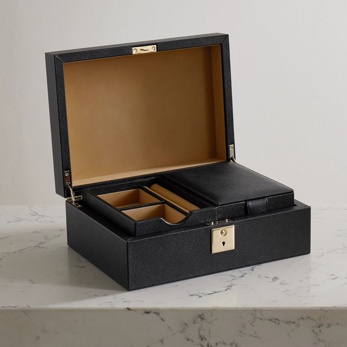 The image showcases an open black leather box with a structured, minimalist design, placed on a white marble surface.