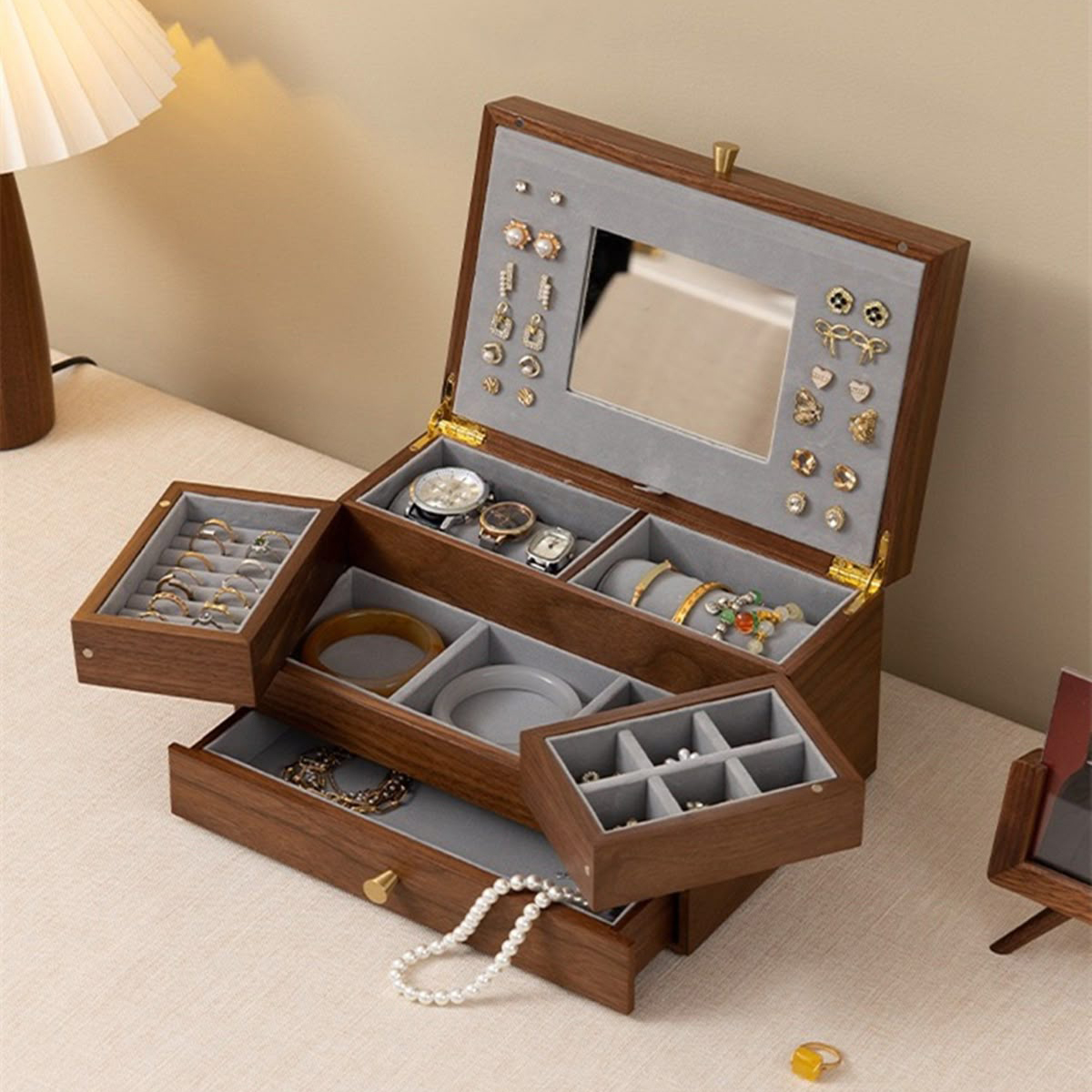 The image shows an open, multi - tiered wooden jewelry box placed on a light - colored surface. 