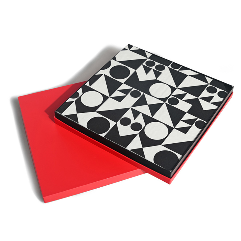 Caja de regalo cuadrada de chocolate rojo con papel protector geométrico blanco y negro sobre la bandeja.