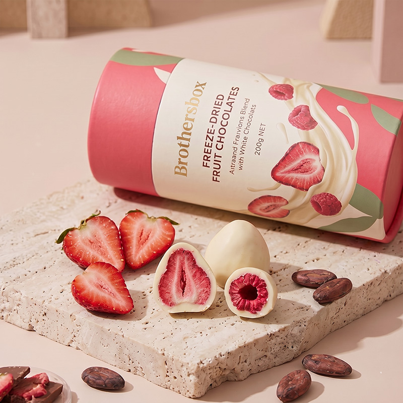 Close up of white chocolate covered freeze dried strawberries next to Brothersbox cylinder box