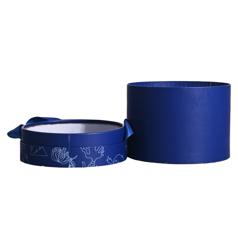 Side profile of an empty open blue cylindrical cake box and its decorative lid placed side-by-side.