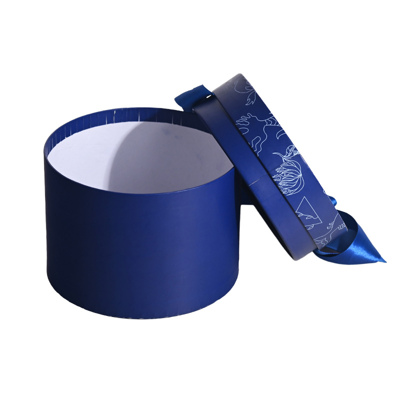 Partially opened dark blue round cake box with the patterned lid leaning against the cylindrical base.