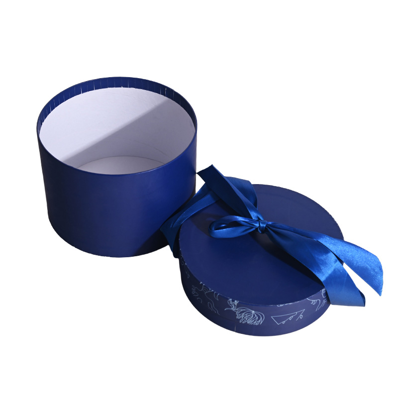 Open blue cylindrical cake box displaying a clean white food-grade interior next to its ribbon-tied lid.